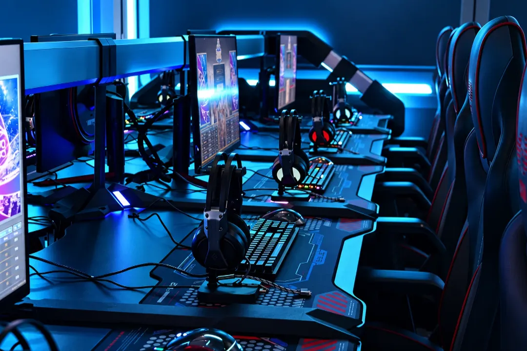 Row of e-sports gaming stations with monitors, RGB keyboards and headsets, lit in blue