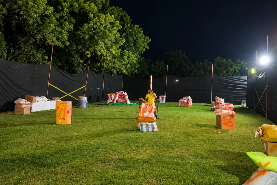 Floodlit paintball arena at night with bunkers on the grass