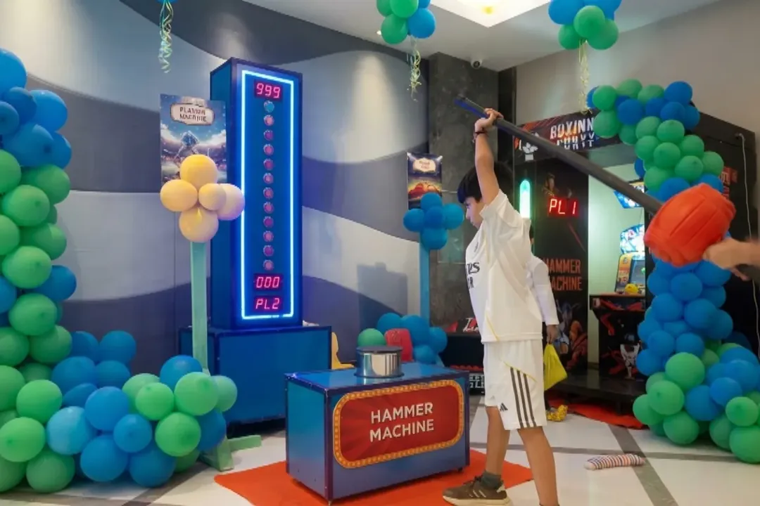 Child swinging a hammer at a rock hammer strength game decorated with balloons