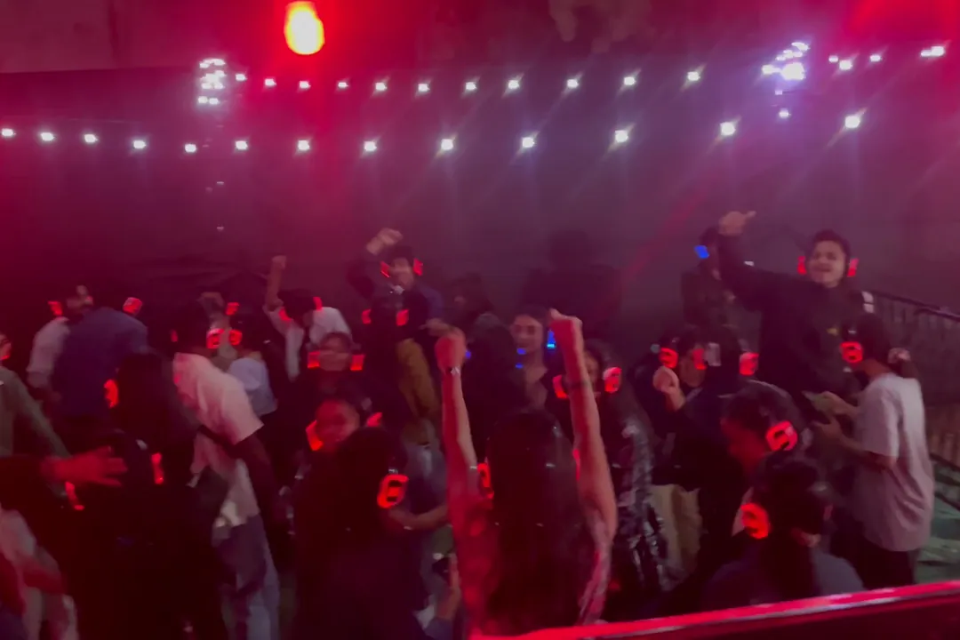 Guests dancing with arms raised behind a barrier at a silent disco, headphones glowing red under white string lights