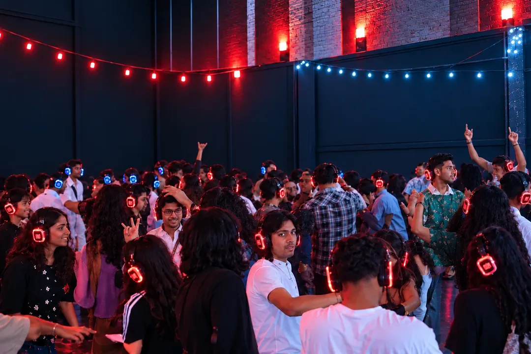 Crowd dancing at a night-time silent disco, guests wearing glowing wireless headphones under string lights
