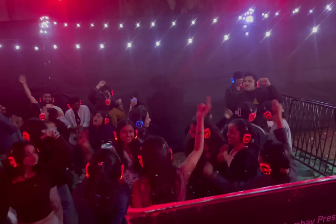 Silent disco crowd dancing in haze under white string lights, headphones glowing red and blue