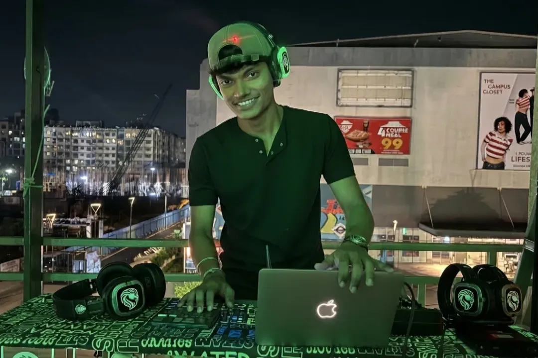 DJ smiling behind a laptop and mixer at a rooftop silent disco setup at night