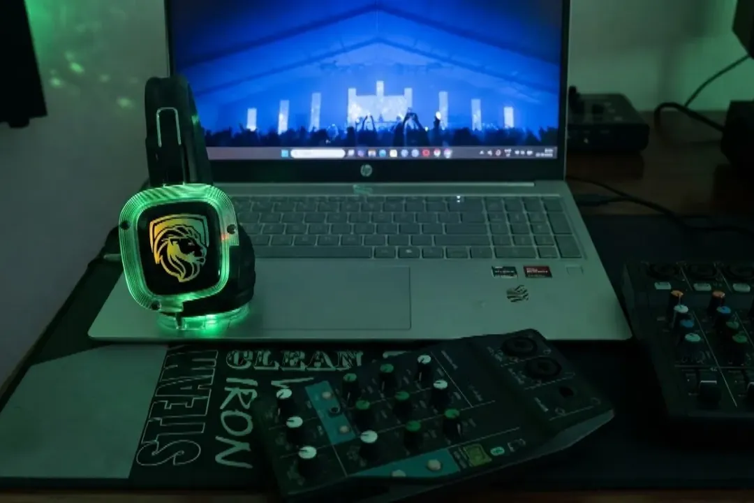 Silent disco DJ station with a glowing wireless headphone resting on a laptop beside audio mixers