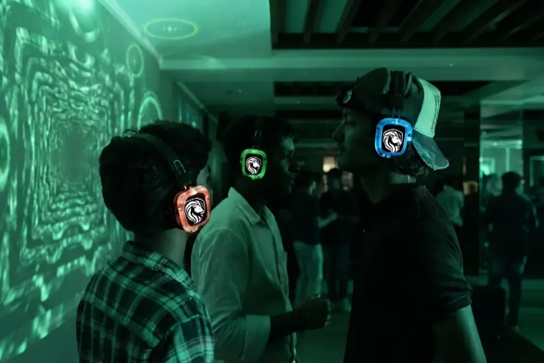 Guests wearing glowing red, green and blue lion-crest wireless headphones at an indoor silent disco lit in green